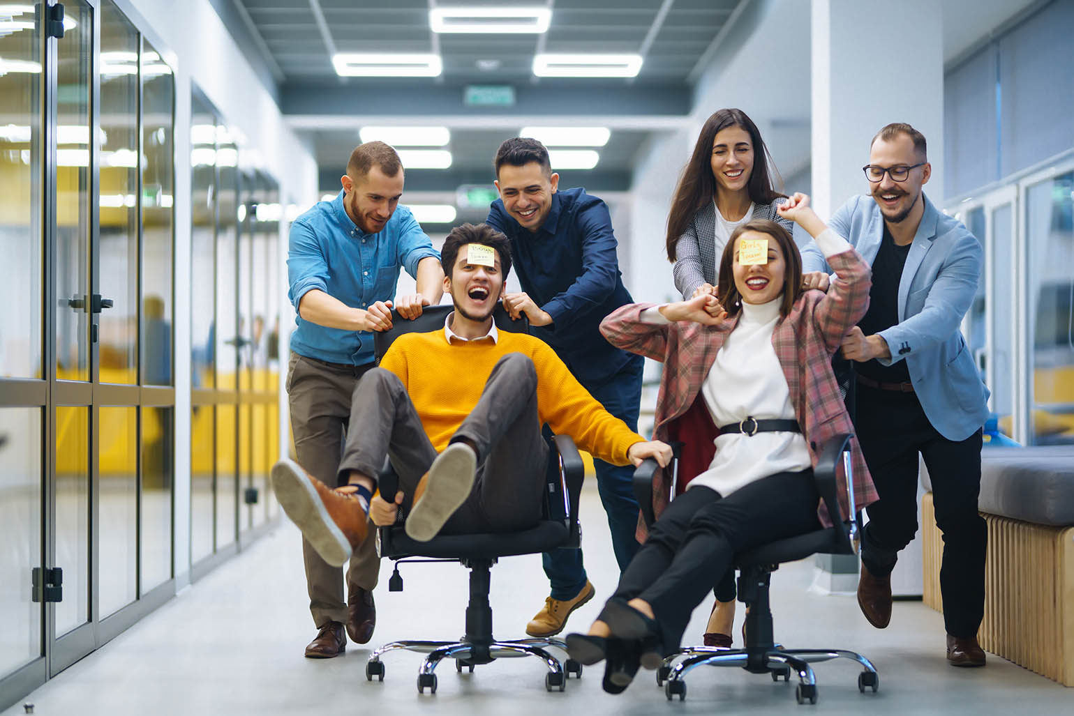 Young cheerful business people racing on office chairs and laughing. Funny activity